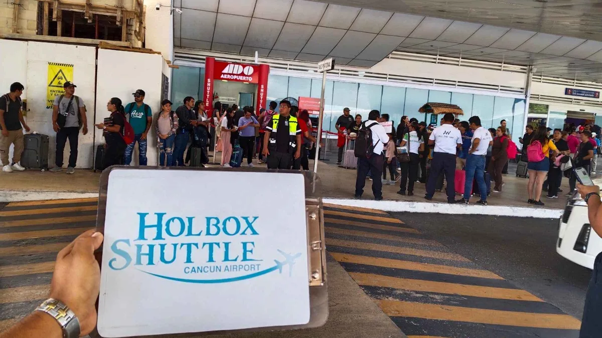 A hand holding a Holbox Shuttle sign in the arrivals area of Cancun airport